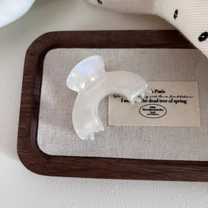 Detail view of small pearlescent acetate hair claw clip on a rustic wooden tray background