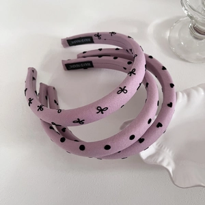 Serre-tête doux en tissu lilas avec motifs de cœurs et nœuds noirs en vue à plat