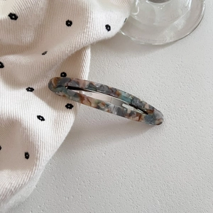 Macro detail of oval marble acetate hair clip with silver stainless steel spring metal base