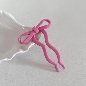 Détail d'une épingle à cheveux rose vif avec nœud et tiges ondulées sur plat en céramique