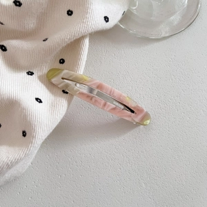 Macro detail of oval acetate hair clip with pink and green marble texture and silver clip