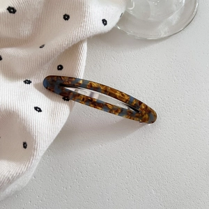 Detail of oval tortoiseshell hair clip with blue patterns and silver metal grip