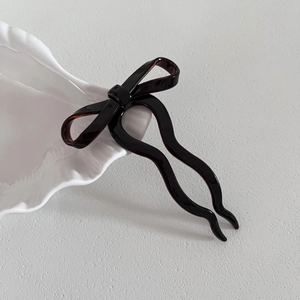 Détail d'une épingle à cheveux ondulée en acétate avec nœud sur un plateau en céramique blanc