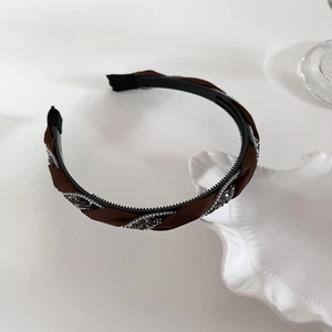 Detail eines geflochtenen Samt-Stirnbands mit grauen Strasssteinen auf weißer Schale