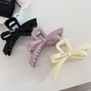 Close-up of bow-shaped hair claw clips in black, lavender, and cream with brand logo
