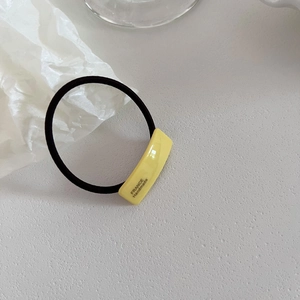 Detail of high-elastic hair tie featuring a yellow acetate rectangle with France Handmade text
