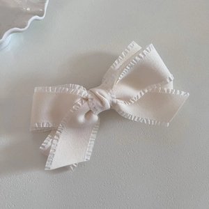 Detailed view of cream-white fabric bow hair clip with elegant pleated edges and soft texture