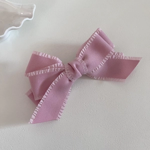 Elegant pink layered bow hair clip with ruffle edges on a minimalist white background