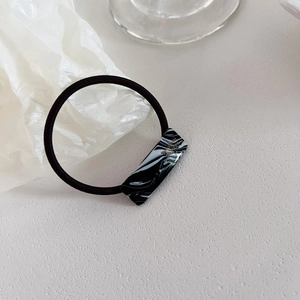 Detail of black elastic hair tie with marble texture acetate square and gold Handmade logo