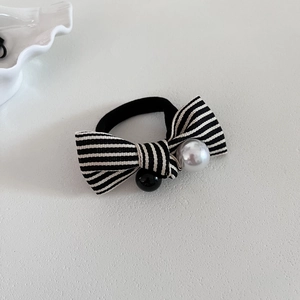 Élastique à cheveux avec nœud rayé noir et blanc et perle sur un bureau blanc