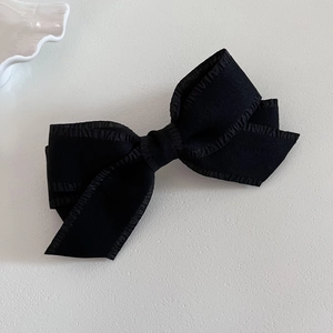 Macro detail of multi-layered black bow hair clip with elegant ruffled edges and texture