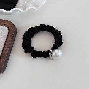 Close-up of black scrunchie with a large elegant white pearl on an off-white surface