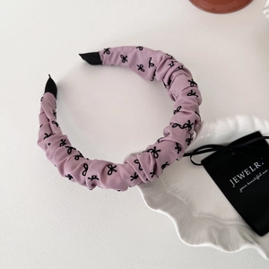 Détail du serre-tête en tissu froncé violet avec motifs de nœuds noirs élégants