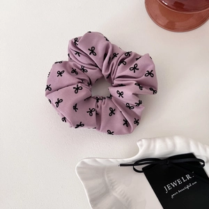 Détail du chouchou lavande avec motifs de nœuds noirs sur un tissu à texture plissée