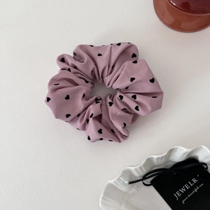 Gros plan sur chouchou en tissu rose avec motif cœur noir et détails plissés