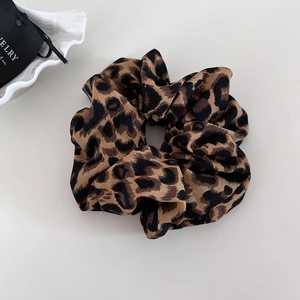 Detailed view of a leopard print satin scrunchie on a minimalist beige background