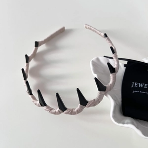 Detail shot of a pink satin padded headband with black punk spikes on a white desk