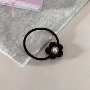 Detail eines schwarzen Haargummis mit Vintage-Perlenblume auf einem Schreibtisch