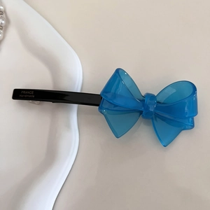 Dettaglio di un fermaglio per capelli a fiocco blu reale con scritta dorata su vassoio bianco