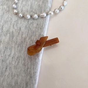 Detail showing amber resin hair clip with France Handmade engraving on grey fabric background