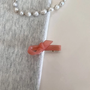 Detail of coral pink bow hair clip with gold logo on soft grey knit fabric