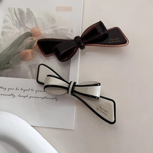 Detail view of two French style bow barrettes in amber and cream with side lettering