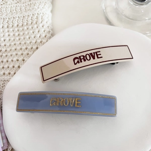 Close-up of retro rectangular hair clips with GROVE lettering in cream and light blue