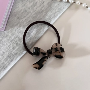 Minimalist tortoiseshell acetate bow hair tie with black elastic band on soft background