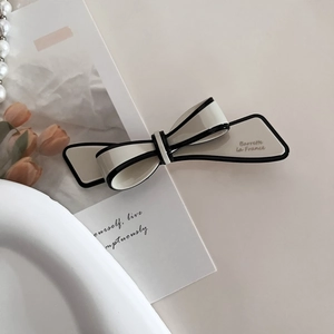 Detail of a creamy white bow hair clip with black edges and Barrette La France text