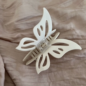 Elegant beige hollow butterfly hair claw clip with metal spring on pink fabric background