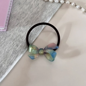 Detailed shot of an iridescent acetate bow hair tie with a black elastic band on soft fabric