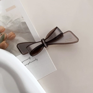 Detail view of translucent taupe bow hair clip with French lettering on minimalist background