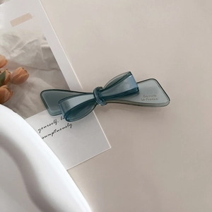 Detailed macro view of the translucent grey-blue bow hair clip on a minimalist beige background