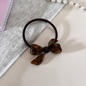 Detail of tortoiseshell acetate bow hair tie with premium elastic band on soft beige background