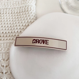 Close-up of cream-colored GROVE letter hair clip on white textured background