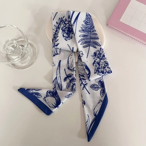 Detailed close-up of a blue floral silk twilly scarf folded on a white ceramic tray