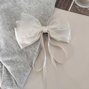 Elegant white mesh and satin bow hair clip with long ribbons on a textured backdrop