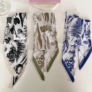 Close-up of three floral print silk scarves in black, green, and blue with pointed ends