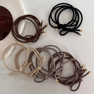 Neutral earth tone braided hair ties set with metallic gold ends on minimalist surface