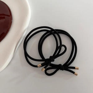 Detail showing two high-elastic black hair ties with polished gold metal cylinders
