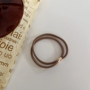 Dettaglio di elastici per capelli marroni a doppio filo con perline dorate su bianco