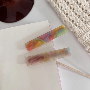 Close-up of square acetate hair clips with colorful marble texture on a soft backdrop