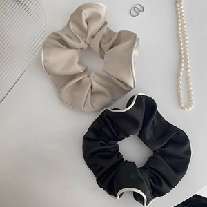 Details von schwarzen und beigen Satin-Haargummis mit elegantem weißem Paspelrand
