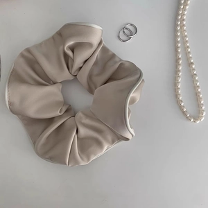 Detailansicht champagnerfarbener Satin-Haargummi mit weißem Saum und seidiger Textur