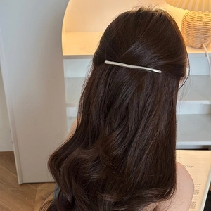 Minimalist silver metal spring hair clip styled on long wavy brown hair in a cozy setting