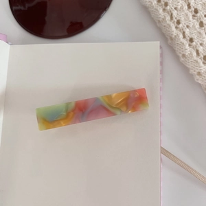 Macro shot of colorful acetate hair claw with iridescent marble texture on cream notebook