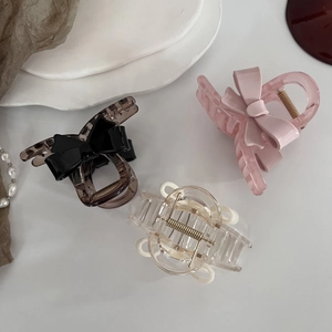 Trois pinces à cheveux en acrylique avec nœuds en marron, rose et crème sur fond blanc