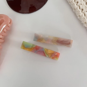 Detail view of two rectangular marble acetate hair claws on a decorative white background