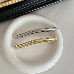 Close-up of gold and silver minimalist polished metal hair clips on a ceramic plate