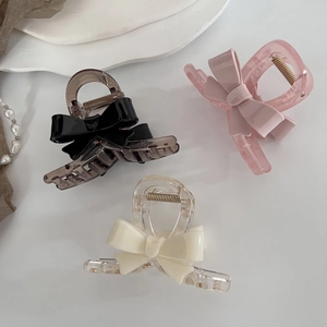 Détail de trois pinces à cheveux en acrylique avec nœuds en noir, rose et blanc crème